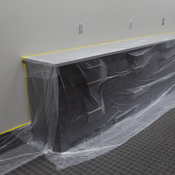 Wall-mounted cabinets and baseboards cover in the pre-taped masking film to protect the furniture from paint during renovations.