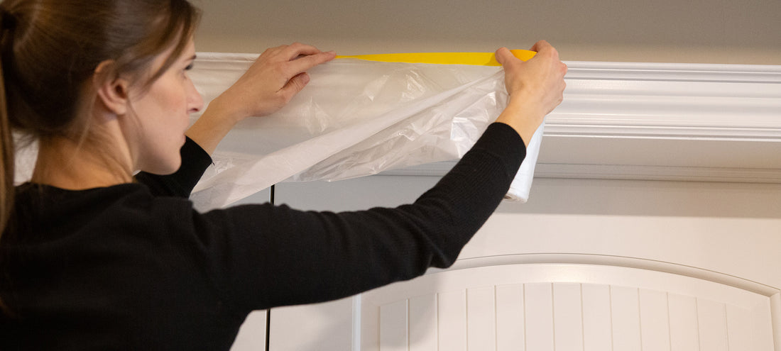 A woman in a black shirt is applying the masking film tape to a white door frame, from left to right.